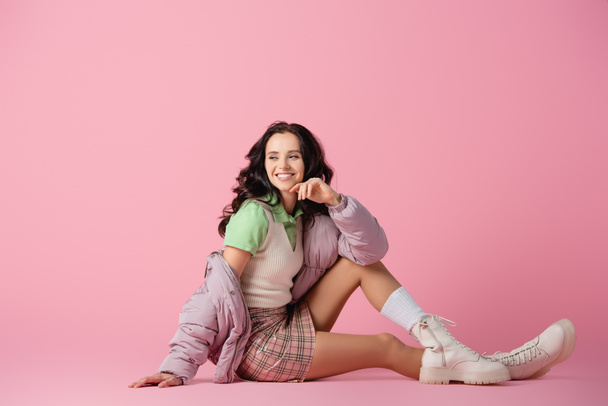 happy brunette young woman in stylish winter outfit posing on floor on pink background - Fotoğraf, Görsel
