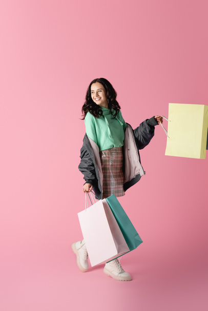 happy brunette young woman in casual winter outfit with shopping bags on pink background - Foto, afbeelding