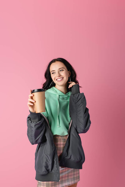 smiling brunette young woman in casual winter outfit with paper cup on pink background - Foto, Imagem