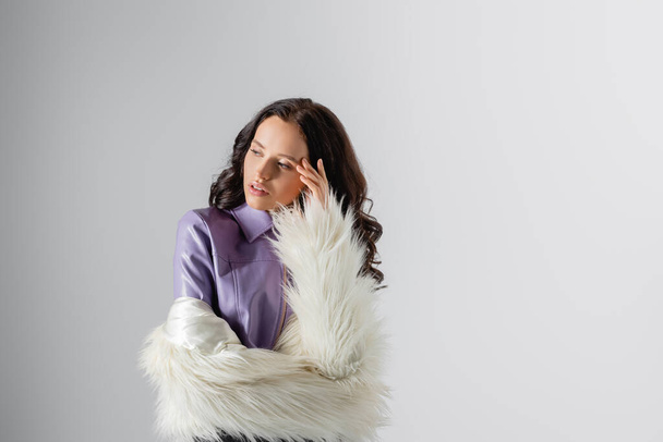 brunette young woman in stylish white faux fur jacket posing on grey background - Photo, Image