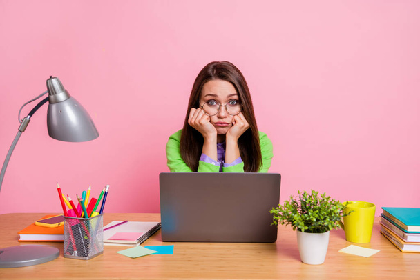 Upset girl sit desk work laptop touch fists cheeks cheekbones wear green shirt isolated pastel color background - Zdjęcie, obraz