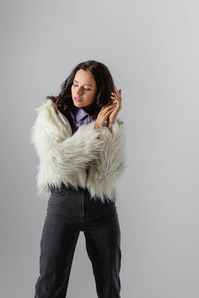 brunette young woman in stylish white faux fur jacket posing on grey background - Fotoğraf, Görsel
