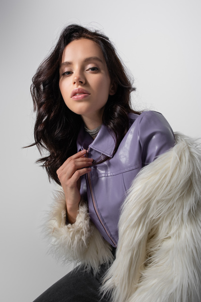 brunette young woman in stylish white faux fur jacket posing on grey background - Foto, afbeelding