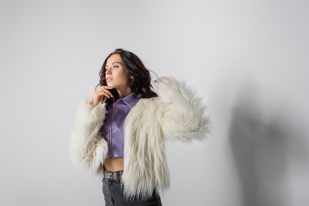 brunette young woman in stylish white faux fur jacket posing on grey background - Foto, immagini