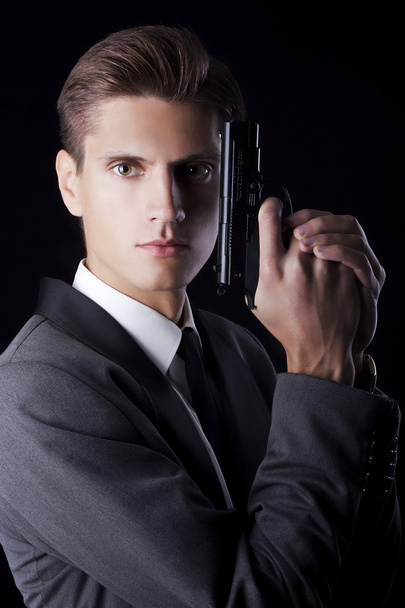 Young attractive macho in suit with gun on black background - Fotoğraf, Görsel
