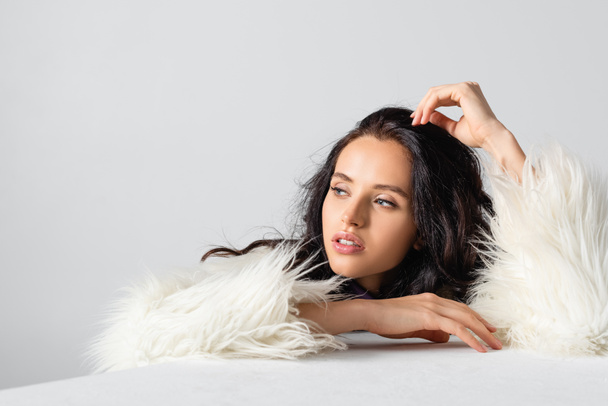 elegant brunette young woman in faux fur jacket posing near cube on white background - Photo, Image