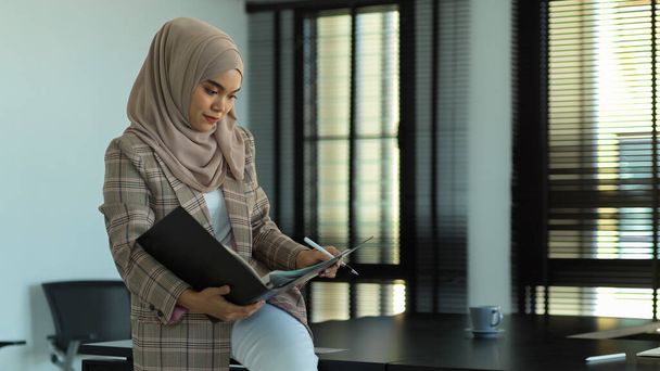 事務室に立ちながら書類を読む若いムスリム実業家の肖像 - 写真・画像