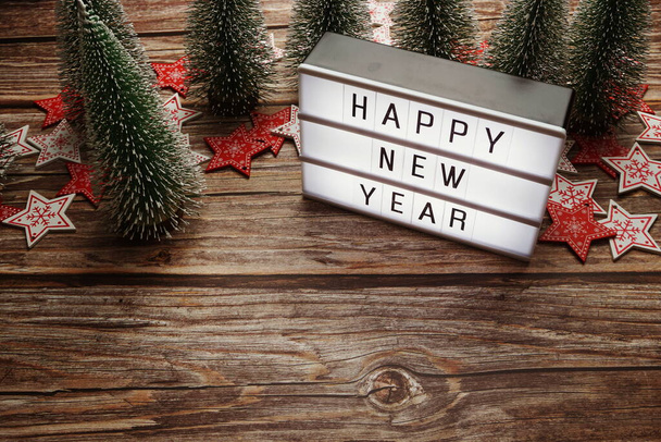 Happy New Year word in light box with Christmas tree decoration on wooden background - Foto, afbeelding