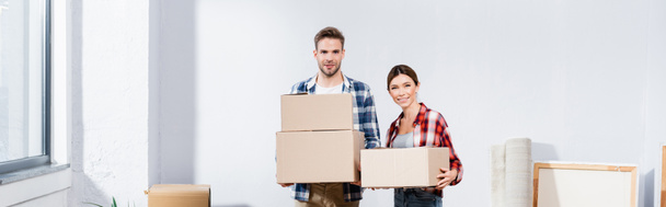 smiling young couple with boxes looking at camera indoors, banner - Foto, imagen