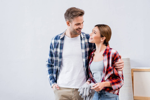 Lächelndes junges Paar schaut einander an, während es sich zu Hause umarmt - Foto, Bild