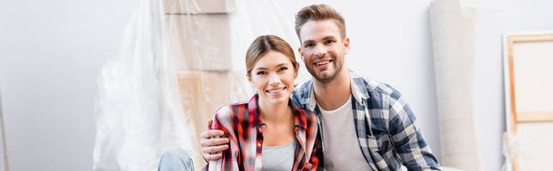 smiling young couple looking at camera during repair at home on blurred background, banner - Foto, imagen