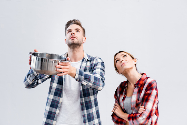 young couple holding pot while looking up under leaking ceiling  - Photo, Image