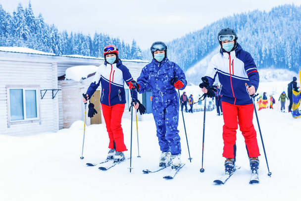 Grupo de amigos felices divirtiéndose. Jóvenes con mascarilla facial durante el coronavirus COVID-19 en una montaña nevada en una estación de esquí - Foto, imagen