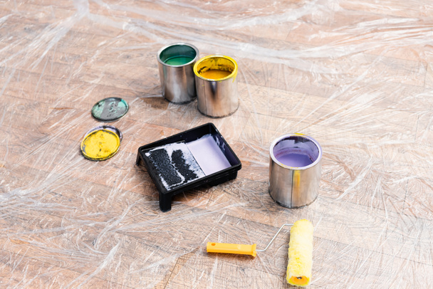 ポリエチレンで覆われた床にローラーとトレイでペイントの缶 - 写真・画像
