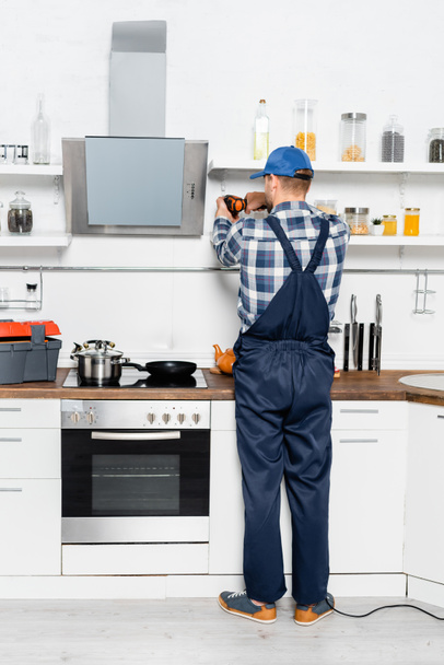 Rückseite des Heimwerkers mit Bohrmaschine zur Reparatur von Regalen in der Küche - Foto, Bild