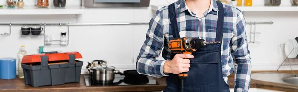 oříznutý pohled na údržbáře držícího vrták na rozmazaném pozadí v kuchyni, banner - Fotografie, Obrázek