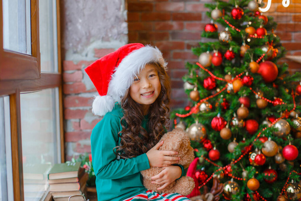 menina asiática em pijama sentado na janela perto da árvore de Natal com Teddy urso Natal, ano novo - Foto, Imagem