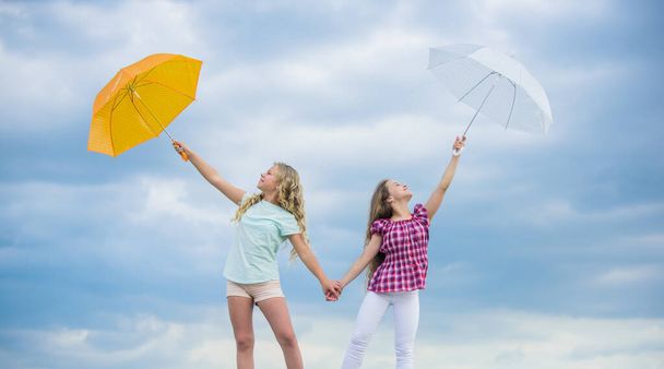 Ready for any weather. Girls friends with umbrellas cloudy sky background. Weather forecast. Weather changing. Carefree children outdoors. Windy or rainy we are prepared. Freedom and freshness - Zdjęcie, obraz