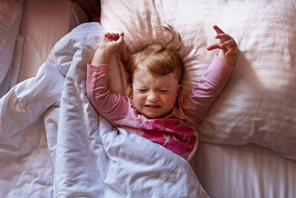 Сонна маленька дівчинка лежить в ліжку і плаче. Ранок час
. - Фото, зображення