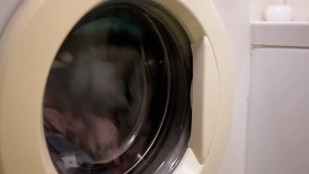 Színes ruhák mosása a háztartási mosógépben. Közelkép. Forgódob - Felvétel, videó