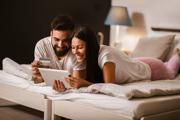 Junges Paar kauft online ein, bequem im Schlafzimmer und mit digitalem Tablet und Kreditkarte - Foto, Bild