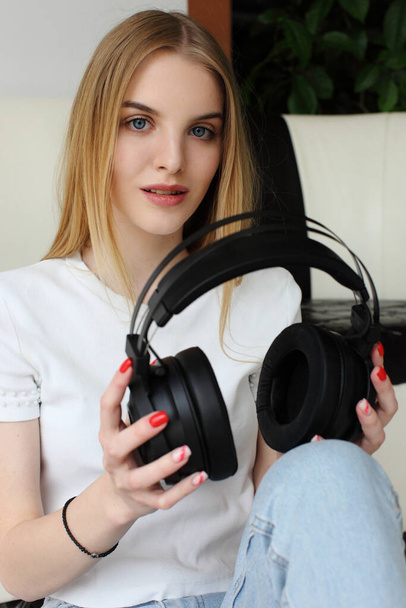 A young woman holds a pair wireless headphones in her hand. - 写真・画像