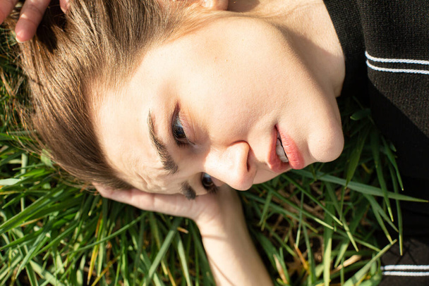 Shiny lying portrait of white girl with dark eyes on green grass - 写真・画像