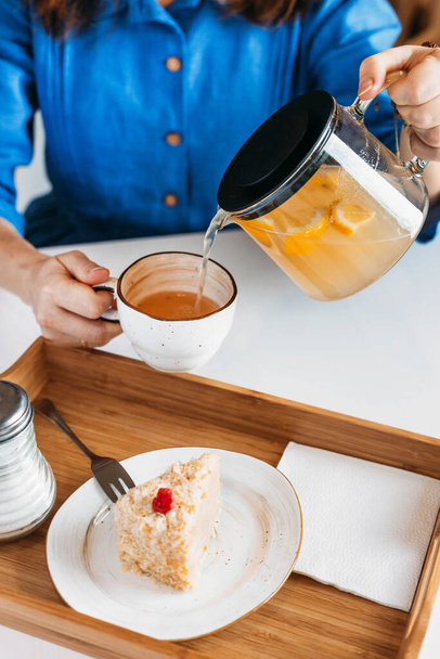 Woman pours herself a healthy lemon tea. For dessert, a piece of cake - Foto, imagen