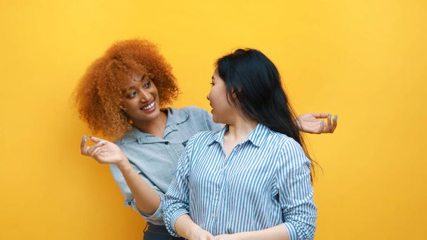 Multiracionális barátság koncepció. Fiatal afro-amerikai fekete és ázsiai nők állnak a sárga fal előtt - Fotó, kép