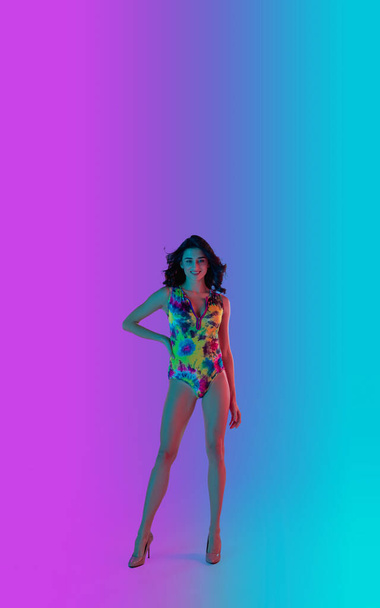Beautiful seductive girl in fashionable bright swimsuit on colour gradient pink-blue background in neon light. - Valokuva, kuva