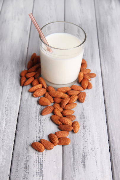 Almond milk in glass with almonds in bowl, on color wooden background - Valokuva, kuva