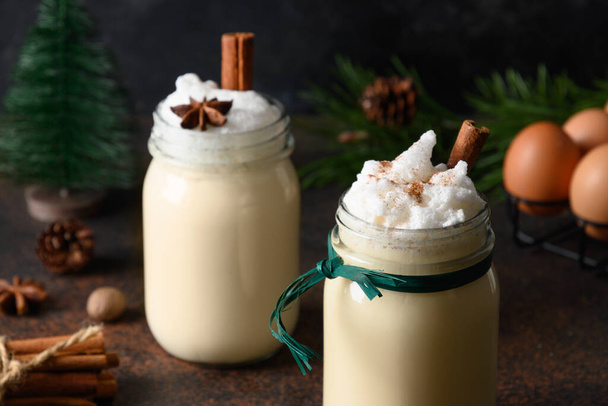 Two holiday Christmas eggnog beverage in mason jar with spices on dark brown background. Close up. - Photo, Image