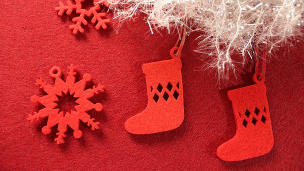 Christmas decoration: christmas tree toy made of red felt in the form of a Christmas sock for gifts. Two socks on a red background with white shiny snow and red felt snowflakes. - Photo, Image