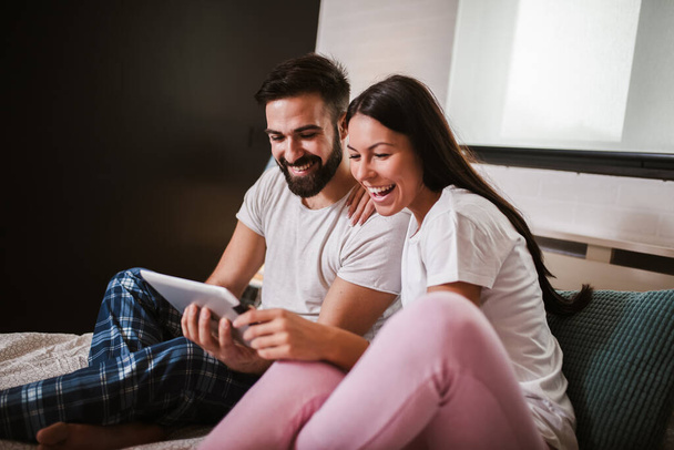 Mosolygó nyugodt fiatal pár segítségével digitális tabletta az ágyban otthon - Fotó, kép