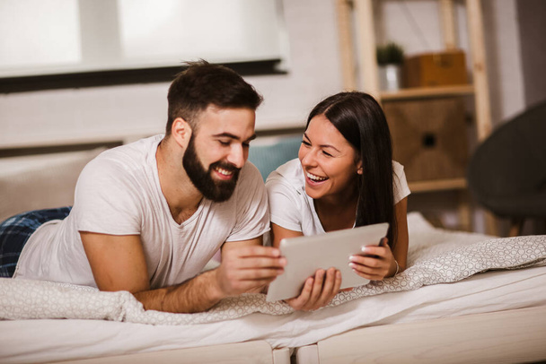 Uśmiechnięta młoda para korzystająca z tabletu cyfrowego w łóżku w domu - Zdjęcie, obraz