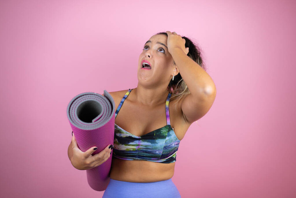 Young beautiful woman wearing sportswear and holding a splinter over isolated pink background putting one hand on her head smiling like she had forgotten something - Foto, Imagem