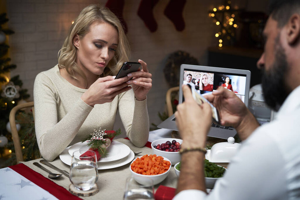 Ζευγάρι που περνούν τα Χριστούγεννα χρησιμοποιώντας το κινητό τηλέφωνο στο τραπέζι                                - Φωτογραφία, εικόνα