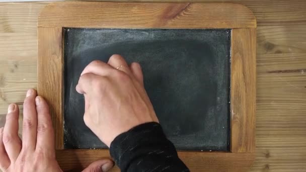 La mano masculina en el tablero escolar en blanco escribe en tiza: 2020! y pone una sonrisa - Feliz - Imágenes, Vídeo