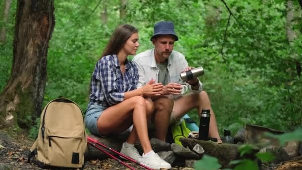 δύο τουρίστες αναπαύονται σε στάση στο δάσος, άνδρες και γυναίκες πίνουν τσάι - Πλάνα, βίντεο
