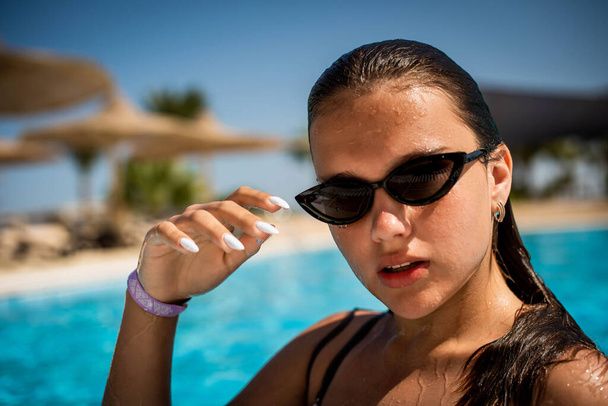 Модний портрет витонченої милої дівчини в стильних сонцезахисних окулярах позує в басейні під час відпустки на розкішному курорті. Веселий плюс розмір дівчина-підліток насолоджується. щасливі, позитивні емоції, літній стиль
. - Фото, зображення
