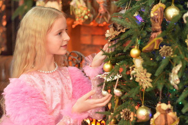 beautiful  girl in pink dress decorating Christmas tree at home - Foto, imagen
