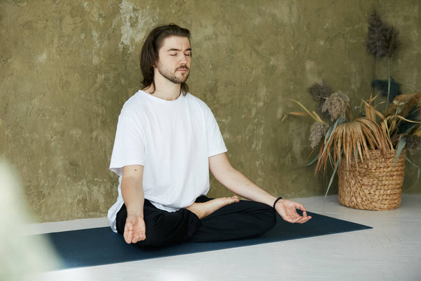 homme concevant dans le yoga asana à la maison, belle personne méditant et attrapant zen sur tapis de yoga - Photo, image