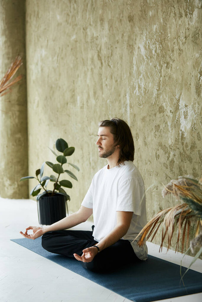 young man with long hair meditating on yoga mat, mindfullness concentration at home, relaxing and calm practice - Foto, immagini