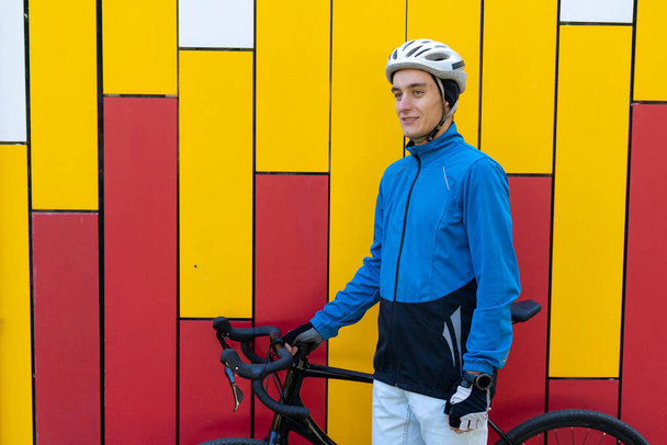 ein junger Mann europäischen Aussehens steht in der Nähe einer hellen Wand mit roten und gelben Streifen. - Foto, Bild