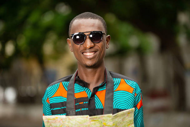feliz joven africano turista de pie con gafas de sol mirando a la cámara sonriendo - Foto, imagen