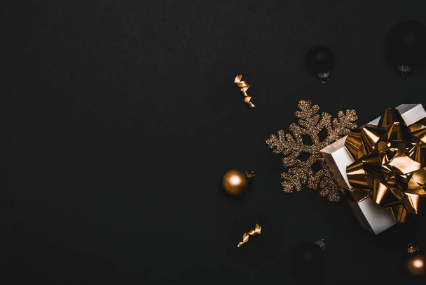 Щасливий Різдво. Біла подарункова коробка з золотою стрічкою, новорічними кульками та блискучою гірляндою у різдвяній композиції на чорному тлі для вітальної листівки. Копіювати простір. Зимові канікули, Новий рік
 - Фото, зображення