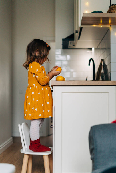 Caucasian girl peeling tangerines on kitchen counter. Healthy child diet. Immune boosting with vitamin c - Foto, Imagem