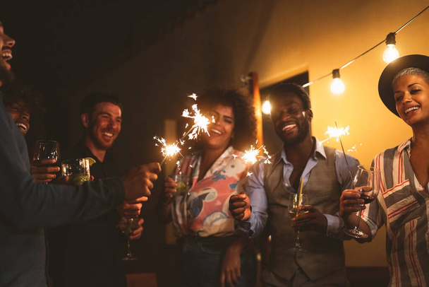 Glückliche junge Freunde feiern Silvester mit Wunderkerzen-Feuerwerk und Cocktails auf Terrassenhausparty - Jugendliches Lebens- und Urlaubskonzept - Foto, Bild