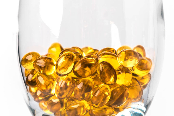 Cápsulas de óleo de peixe omega-3 amarelo ou vitamina D em um copo de vidro transparente em um backgroun branco - Foto, Imagem