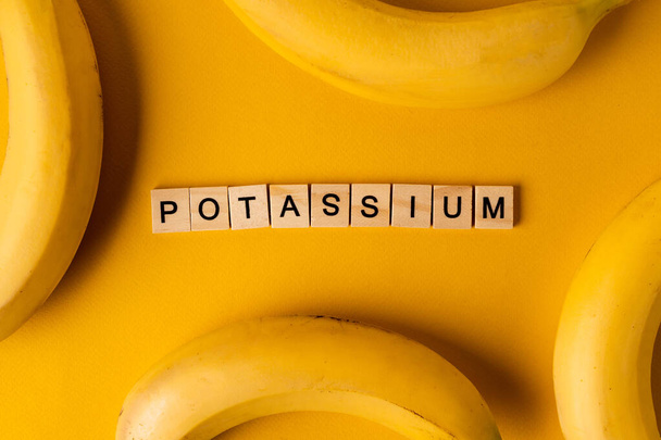 A palavra "Potássio" é colocada fora de blocos de madeira no meio de bananas em um fundo amarelo. O conceito de um estilo de vida saudável - Foto, Imagem